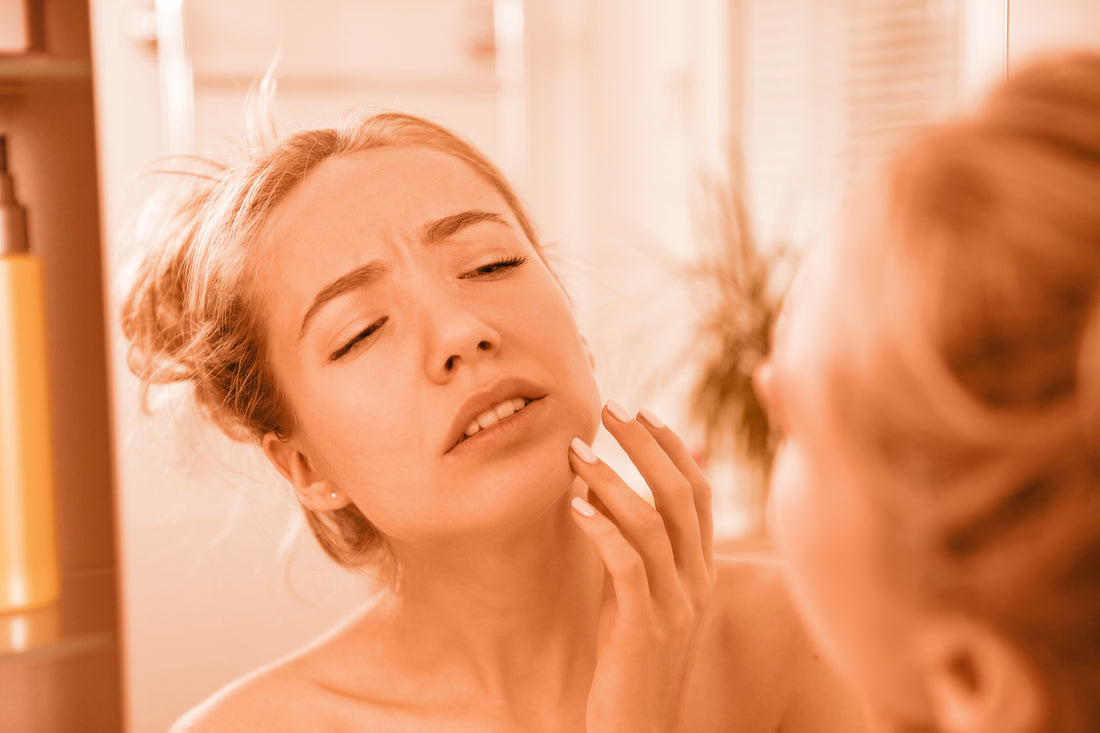 Woman looking in the mirror at a pimple on her face
