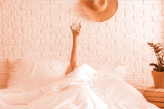 Woman laying in bed holding a glass up